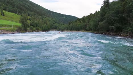 Luftaufnahme-Eines-Kajakfahrers,-Der-Durch-Wildwasser-Stromschnellen-Durch-Einen-Malerischen-Fluss-Navigiert,-Der-Von-üppigem-Grün-Und-Bergen-Umgeben-Ist