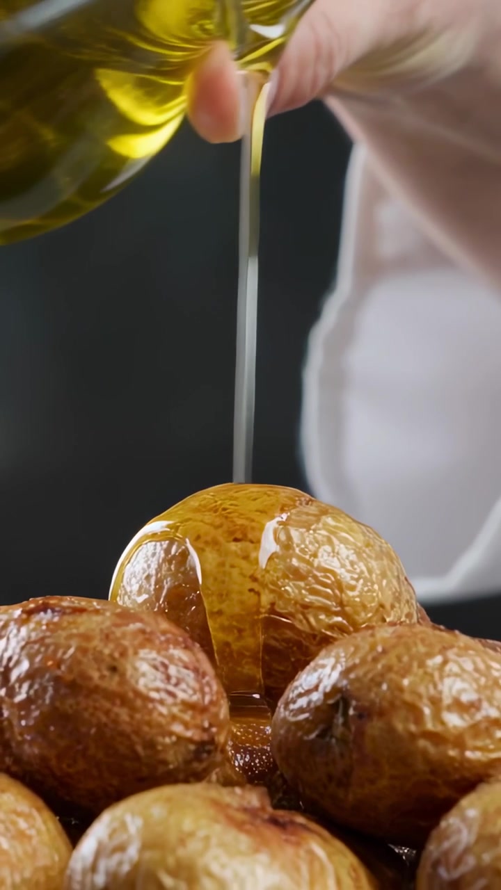 Video verticale: Cuoco in camicia che versa l'olio inclinando un versatore sulle patate in cucina per impiattare.