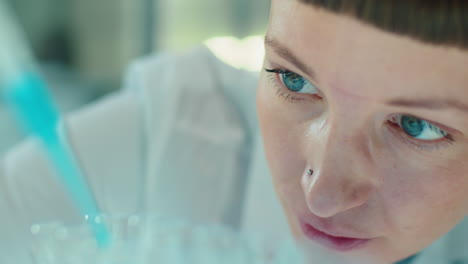 female lab scientist pouring blue liquid substance with pipette
