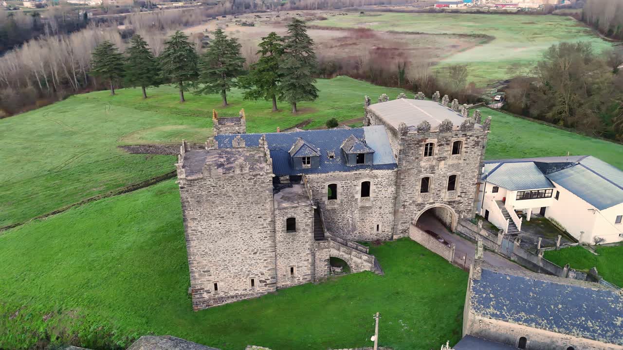 Aerial shot of Arnedo Castle, a historic stone fortress with towers and archways, surrounded by green fields and trees in Valdeorras.