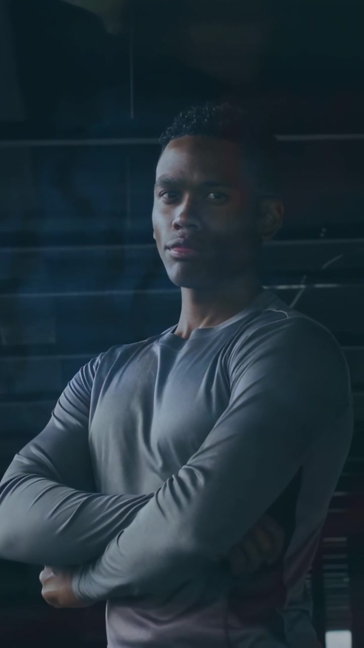 Folding adult man moving into crossed arms in gym wearing grey top, glass glare, camera tightening