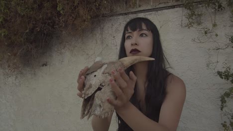 Circular-view-of-serious-woman-with-long-black-hair,-showing-the-skull-of-an-animal-with-horns