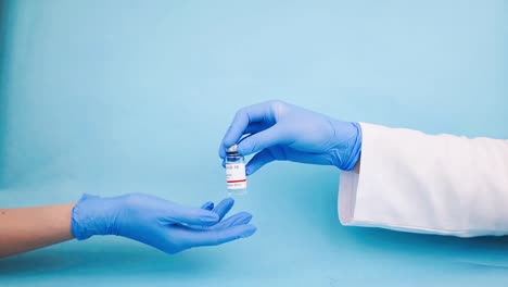 Arzt-übergibt-Das-Covid-19-Heilmittel-An-Eine-Krankenschwester,-Coronavirus-impfkonzept-Auf-Blauem-Hintergrund