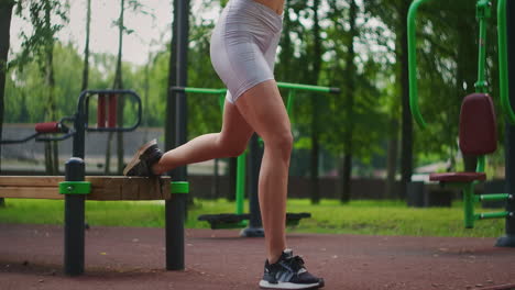 a young beautiful woman alone performs exercises in the park in the summer on a bench. healthy lifestyle and sports training in the park in summer.