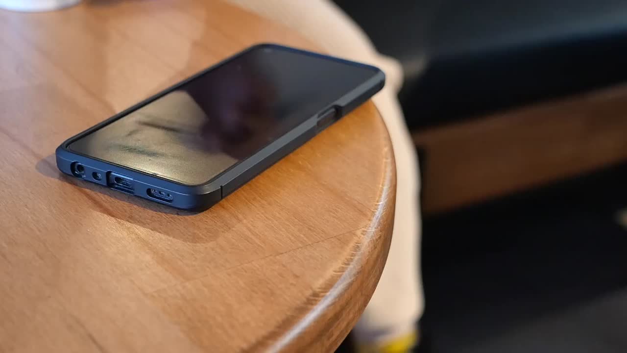 A hand reaching for a smartphone on a wooden table