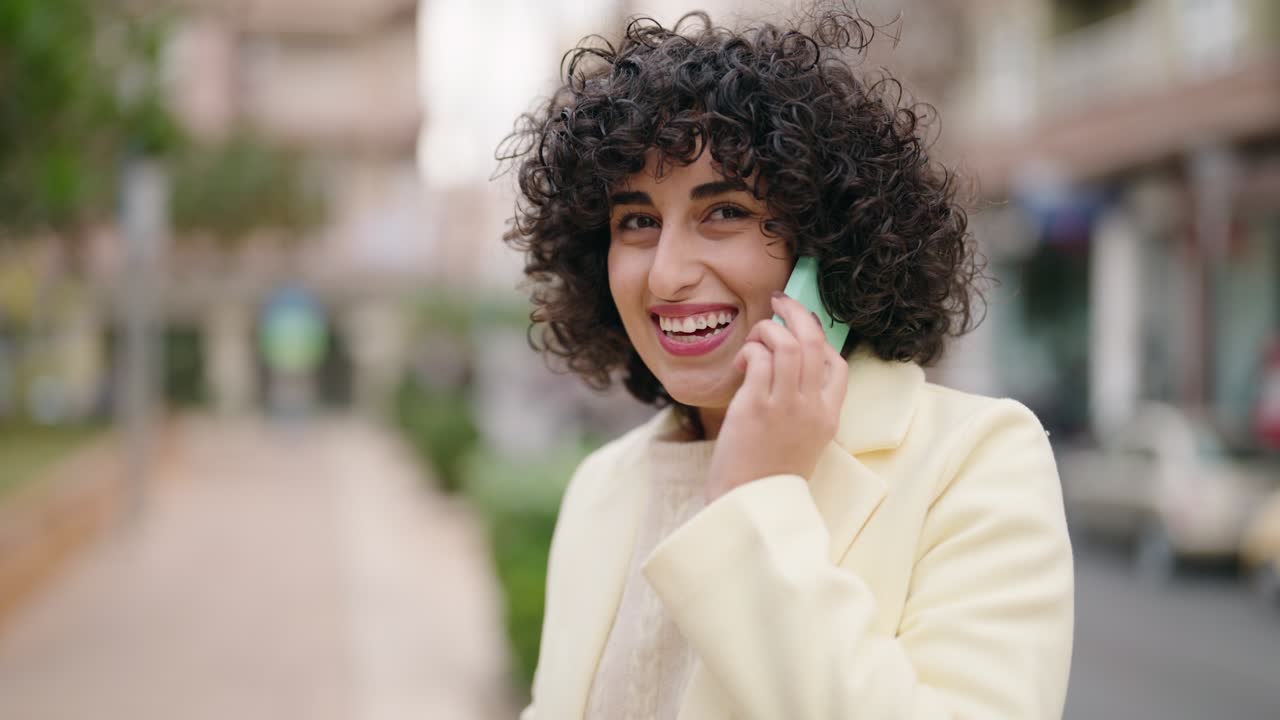 mujer joven sonriendo confiada hablando en el teléfono inteligente en la calle