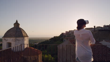 mujer usando auriculares de realidad virtual en el balcón mirando a su alrededor disfrutando de la experiencia explorando el ciberespacio en línea en un hermoso fondo de puesta de sol