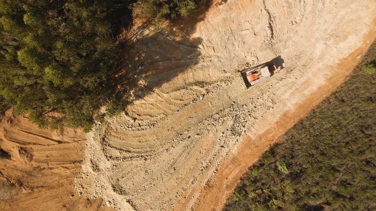 4K luftfoto af en bulldozer, der flytter jord midt i skoven.