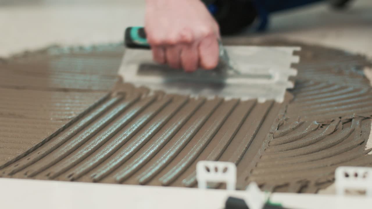 Construction worker spreading tile adhesive on a floor of a house in renovation
