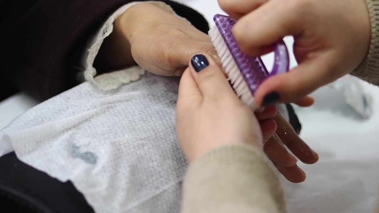 Manicurist Cleaning Client's Fingernails with Brush in Salon