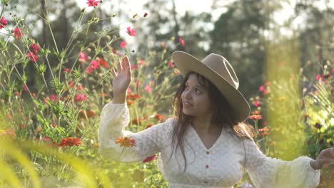 little girl with glasses, hat and white dress spinning and smiling very happy in a field of zinnia flowers, during sunset