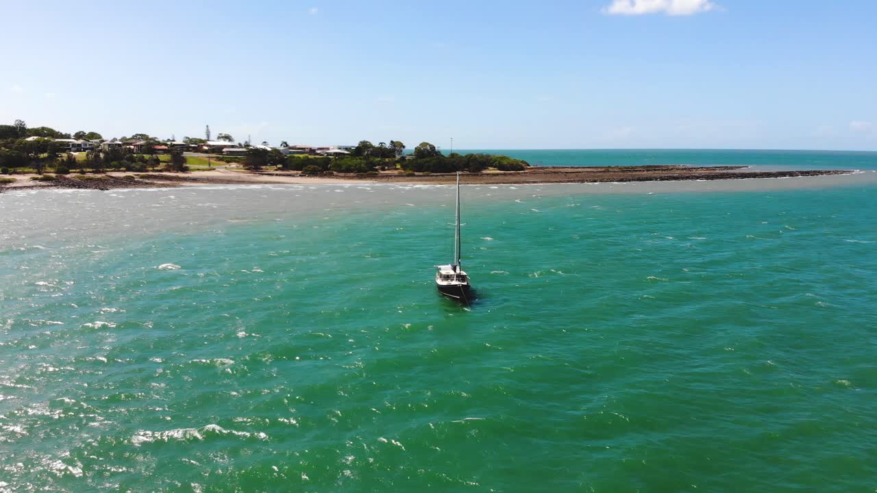 dando vueltas alrededor de un pequeño bote de vela que flota en el agua tropical, azul demin y verde esmeralda justo debajo de la costa, mientras que un cielo azul con nubes blancas esponjosas de tamaño mediano flota arriba