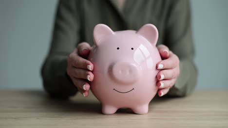 hands protecting a pink piggy bank