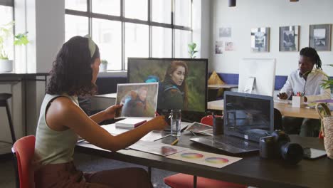 mujer de negocios biracial trabajando con una computadora portátil y sosteniendo una foto en la oficina