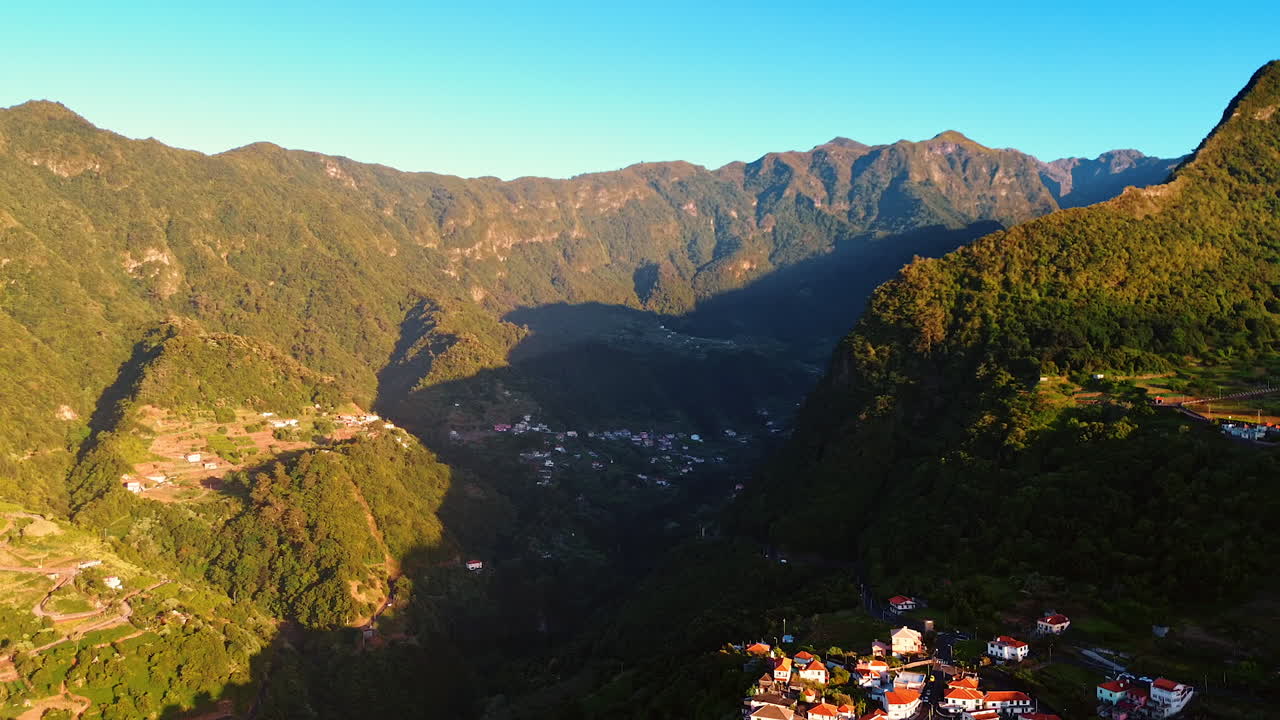 Picturesque huge mountains hide a cozy town. Amazing scenery of the mighty rocks at the Madeira Islands, Portugal. Aerial view.
