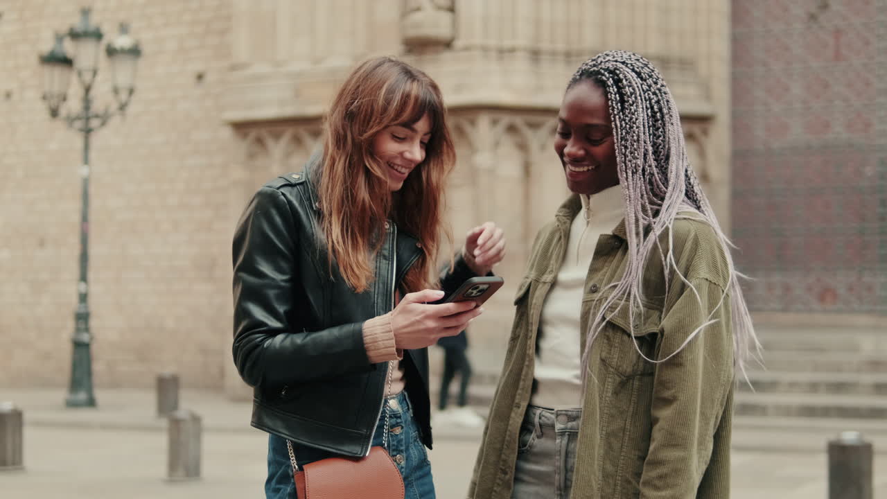 Two Happy Young Women Looking at Smartphone and Laughing in City