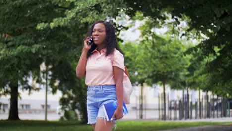 Concepto-De-Tecnología,-Educación-Y-Personas-Feliz-Y-Sonriente-Estudiante-Afroamericana-Con-Libros-De-Texto-Llamando-A-Un-Teléfono-Inteligente-En-La-Ciudad