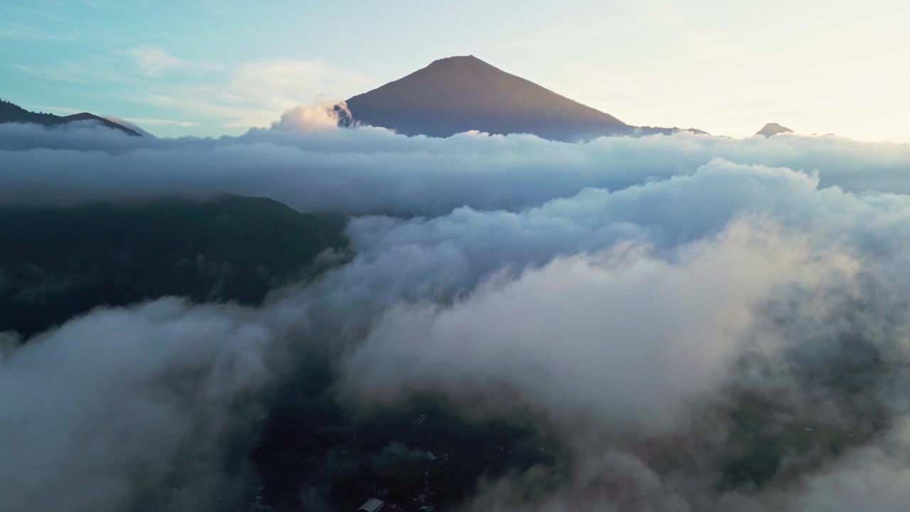 Montagna vulcanica che si erge sopra un vasto mare di nuvole con una spettacolare inversione nuvolosa e valli coperte di nebbia durante un'alba dorata, riprese aeree con drone