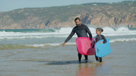 surfer with artificial leg and daughter holding surfboard and talking while walking on the beach 1