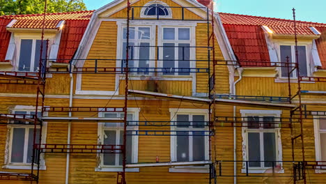 Static-shot-of-renovation-work-going-of-an-old-wooden-cottage-with-beautiful-red-roof-on-a-bright-sunny-day-in-timelapse