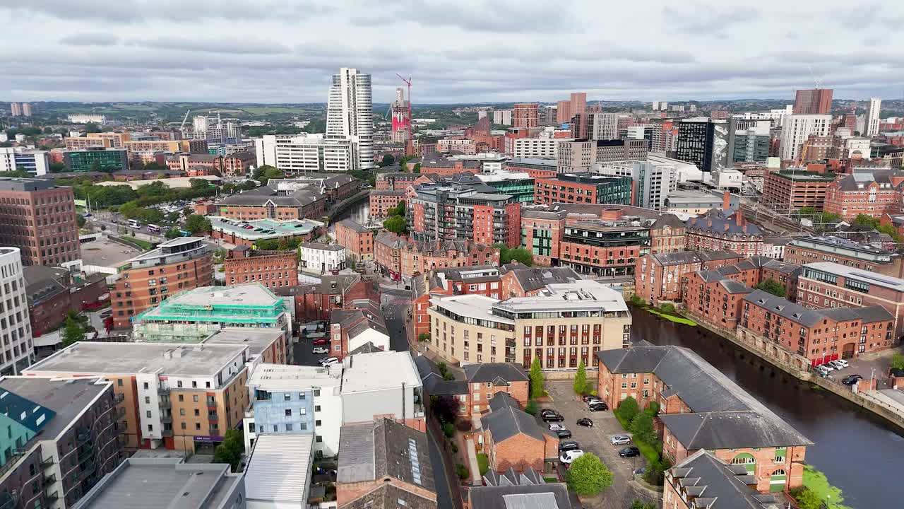High-angle aerial footage pans across a vibrant cityscape with Victorian buildings, a winding river, and modern structures under bright, diffused daylight