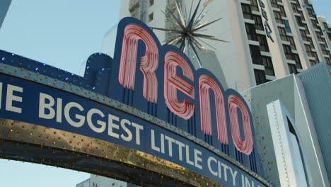 a dynamic shot begins at the iconic reno arch, then smoothly transitions to reveal a vibrant rock climbing wall behind it, showcasing the city's adventurous spirit during the bright daytime.