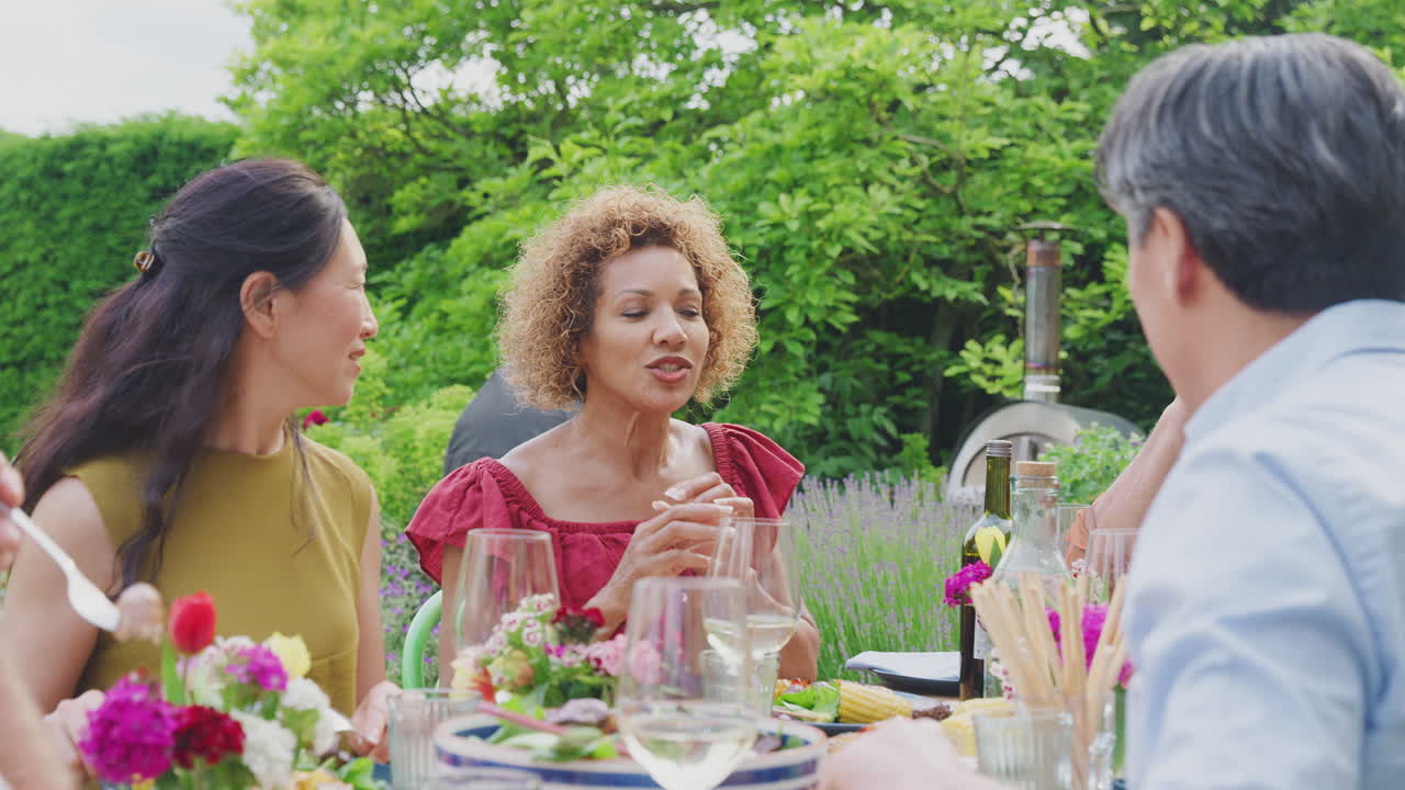 grupo de amigos maduros hablando alrededor de la mesa en la fiesta de cena de verano en el jardín en casa