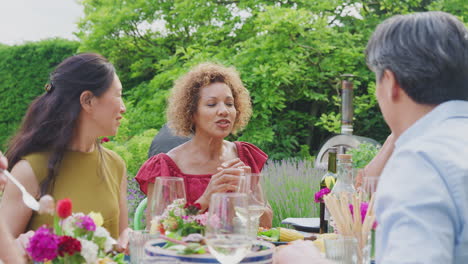 group of mature friends talking around table at summer dinner party in garden at home