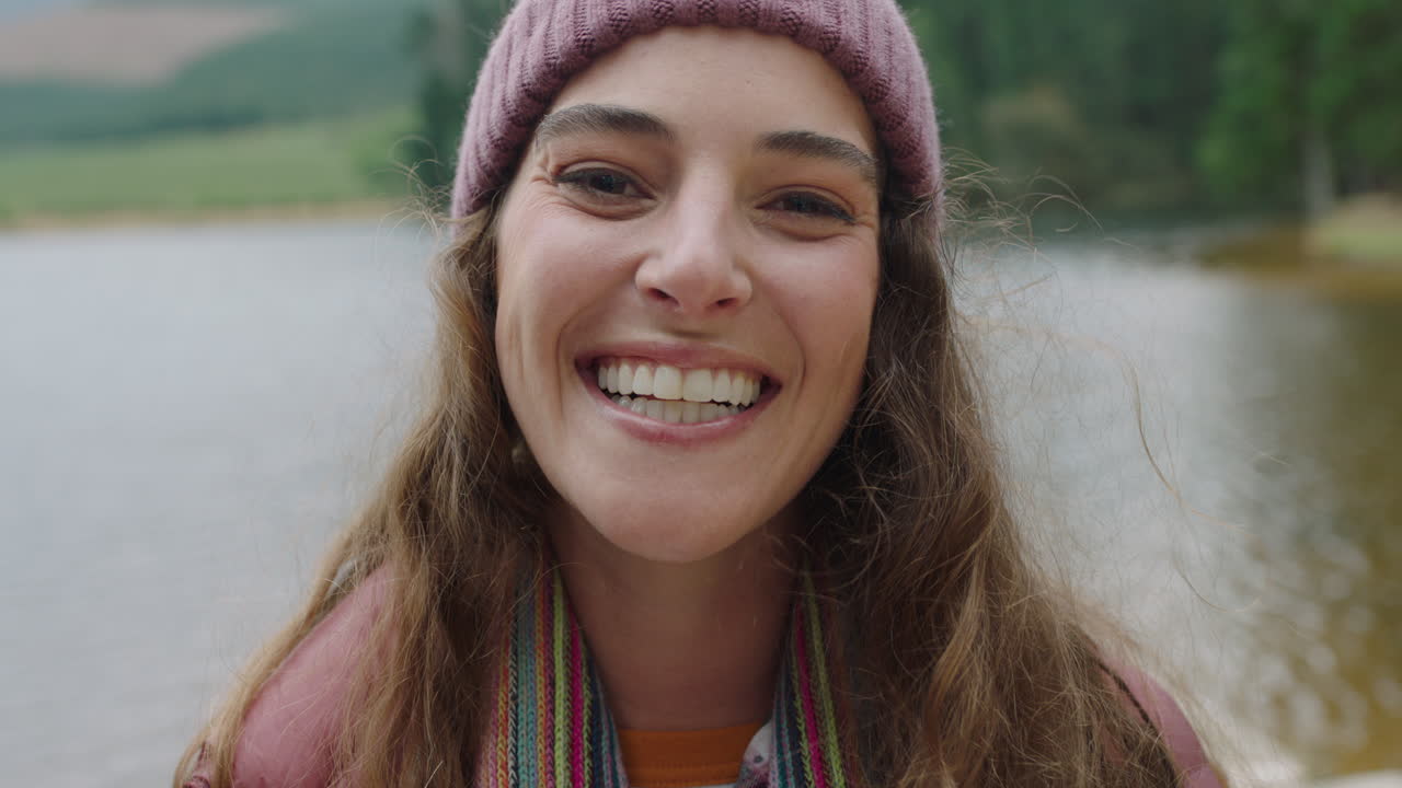 retrato mujer feliz sonriendo sintiendo alegría usando gorro disfrutando del frío invierno al aire libre en la naturaleza junto al lago gente real 4k