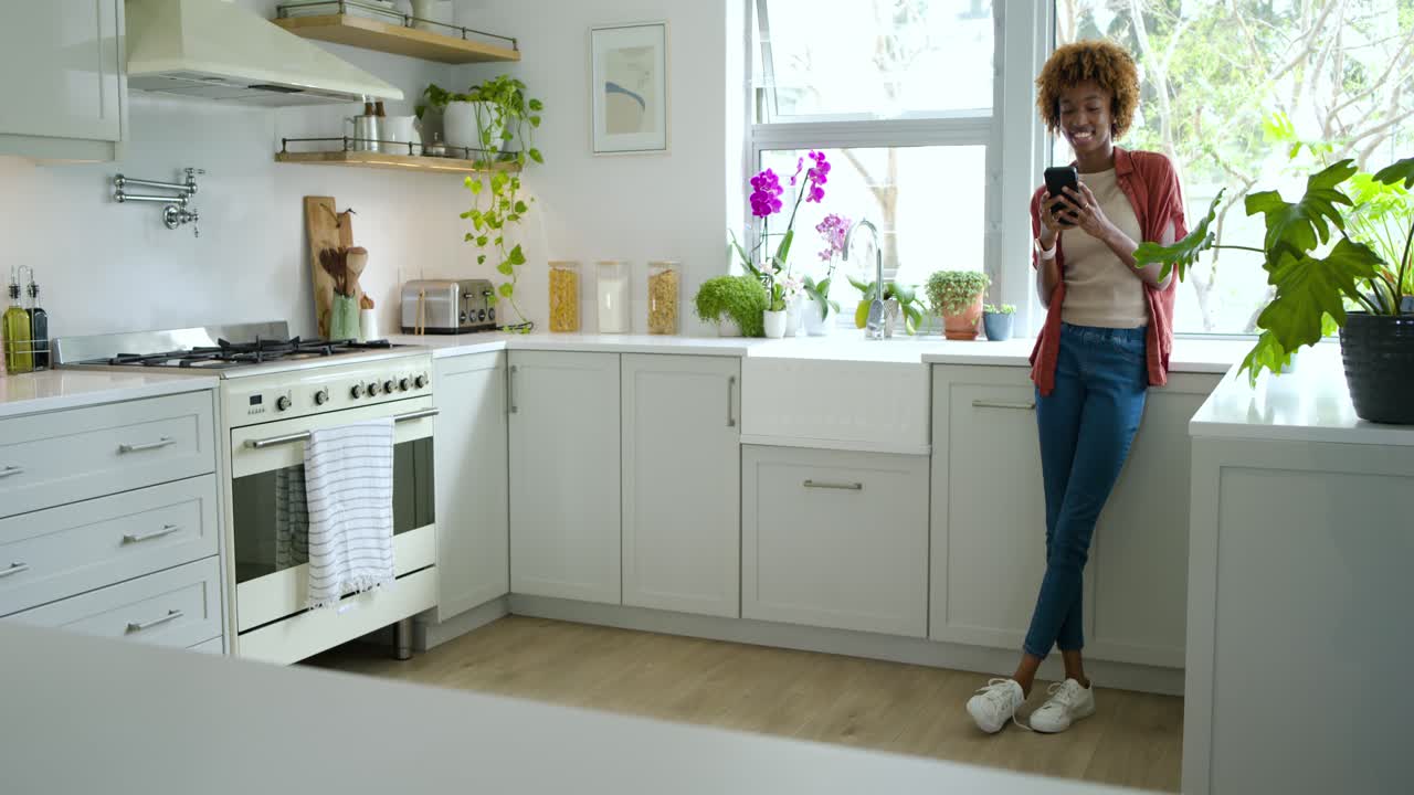 Donna afroamericana adulta che entra in cucina dopo un segnale, scorrendo il telefono e sorridendo, con spazio per il testo