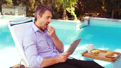 Handsome-man-using-tablet-on-deck-chair-and-eating-fruit