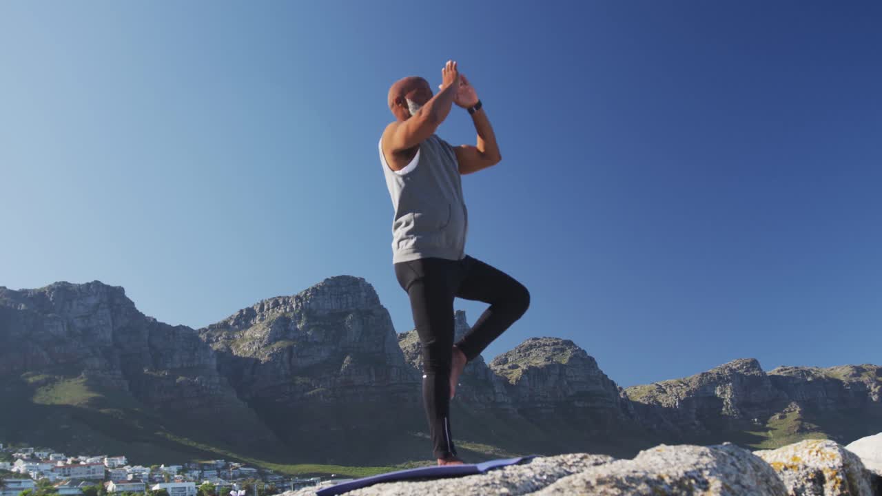 시니어 아프리카계 미국인 남자가 바 ⁇ 가의 바위 위에서 스트레칭을 하고 있습니다.