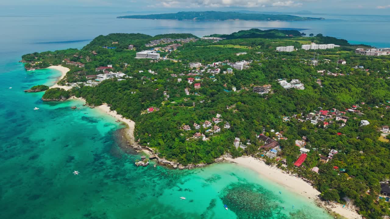 Drone riprende la costa di un'isola con mare blu, case locali e resort sulla spiaggia