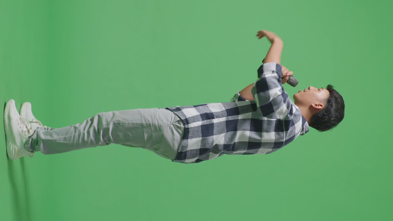 녹색 스크린 배경에서 마이크를 들고 하는 젊은 아시아 십대 소년의 전체 몸 측면 시각