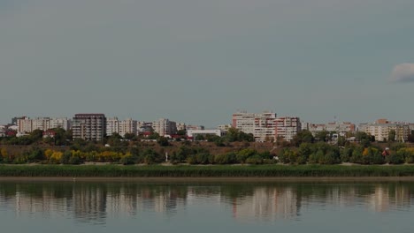 Low-flying-drone-shot,-flying-above-a-big-river,-revealing-a-portion-of-the-city's-skyline-mirrored-in-the-glistening-water-4K60Fps