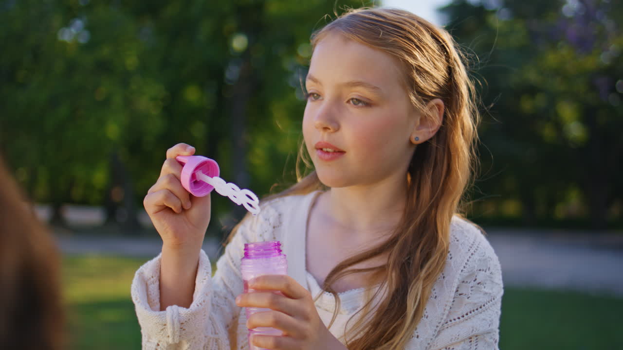 Child playing soap bubbles in sunny park portrait. Cute kid enjoying childhood