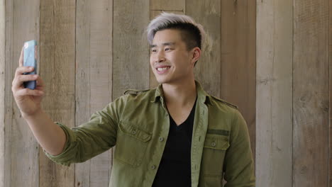 portrait-of-young-handsome-asian-man-student-smiling-posing-taking-selfie-photo-using-smartphone-camera-technology-wooden-lobby-background