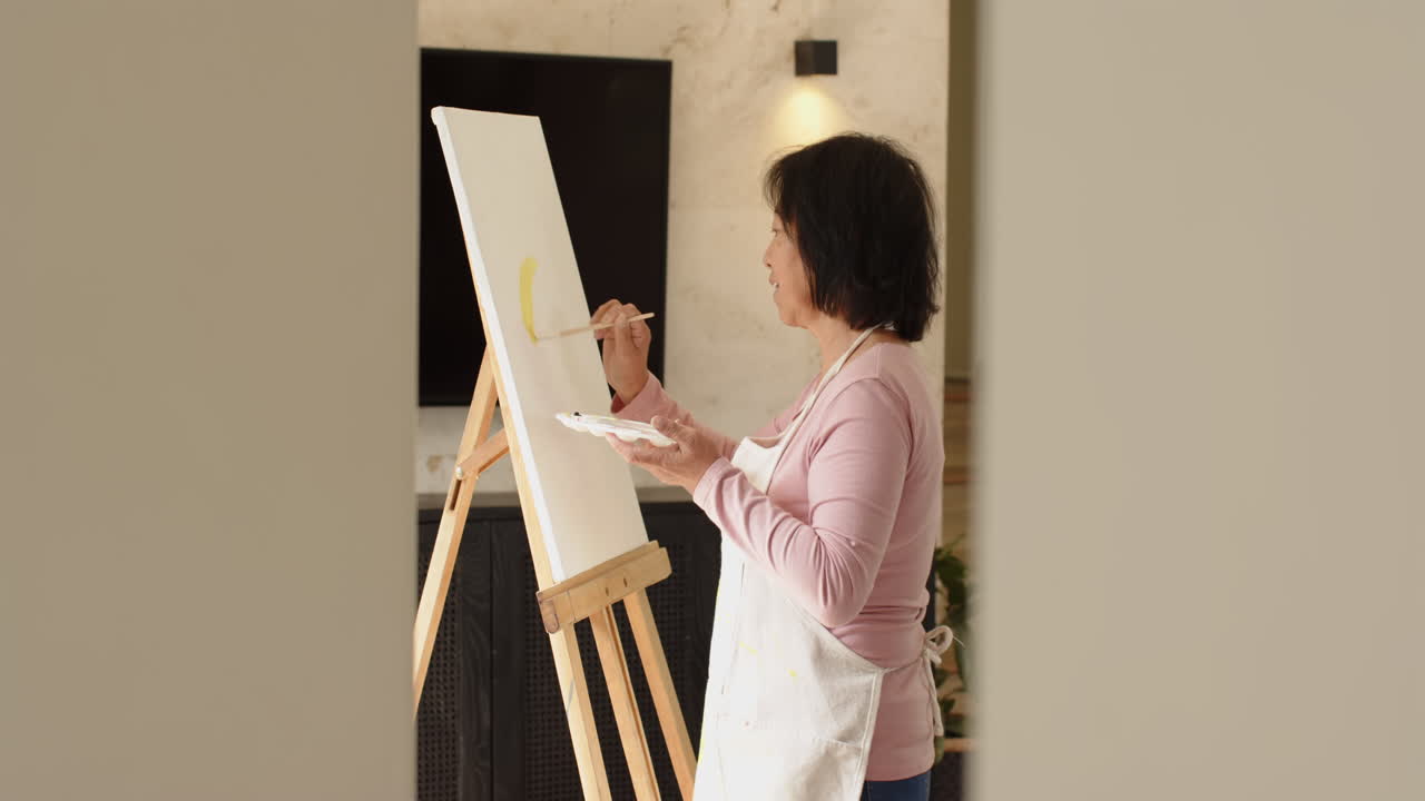 Senior woman painting on canvas at home, enjoying creative solitude