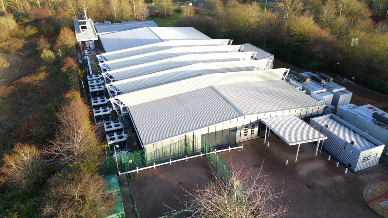 Drone view of high-tech AI data processing hub in Milton Keynes featuring advanced external cooling fan arrays.