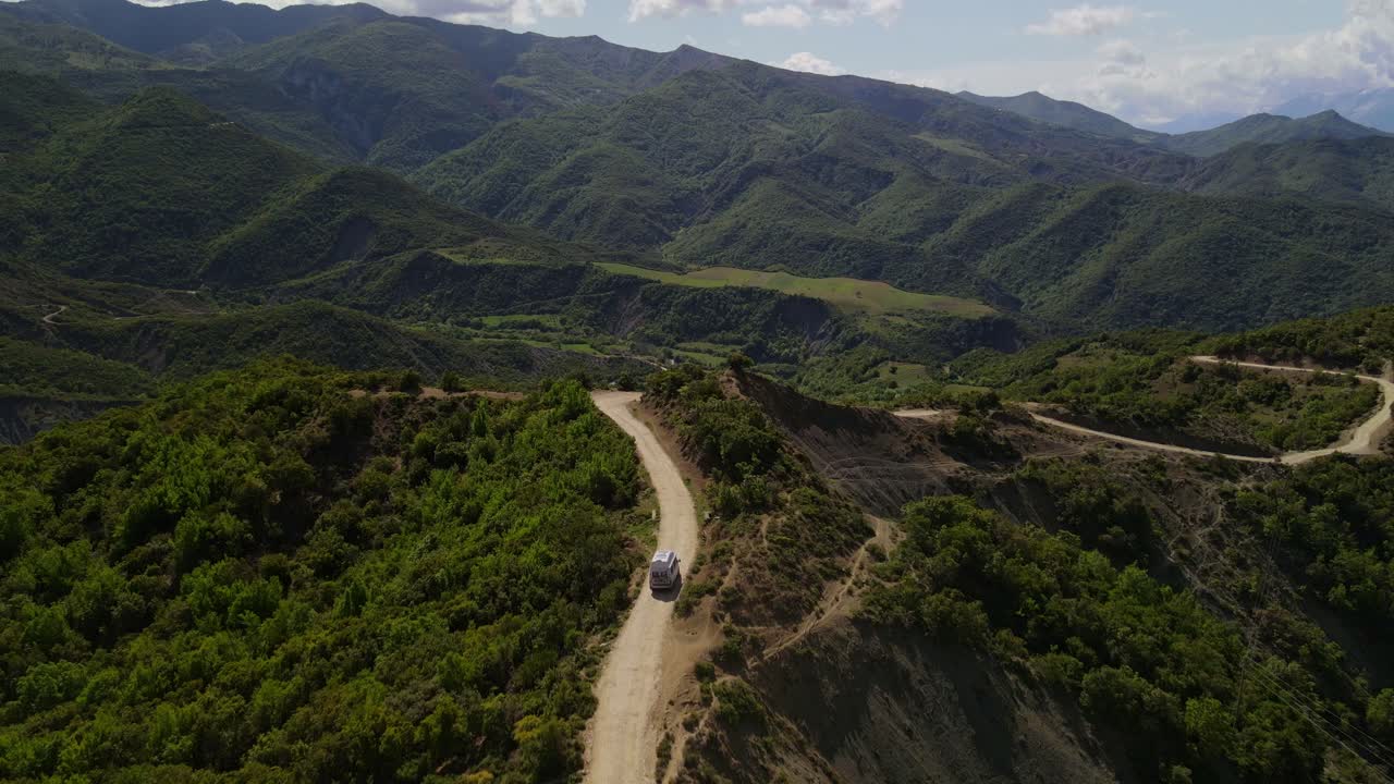 imágenes de drones volando sobre una autocaravana conduciendo a lo largo de un sinuoso camino de tierra en la cadena montañosa trebeshinë-dhëmbel-nemërçkë cerca de permet, albania