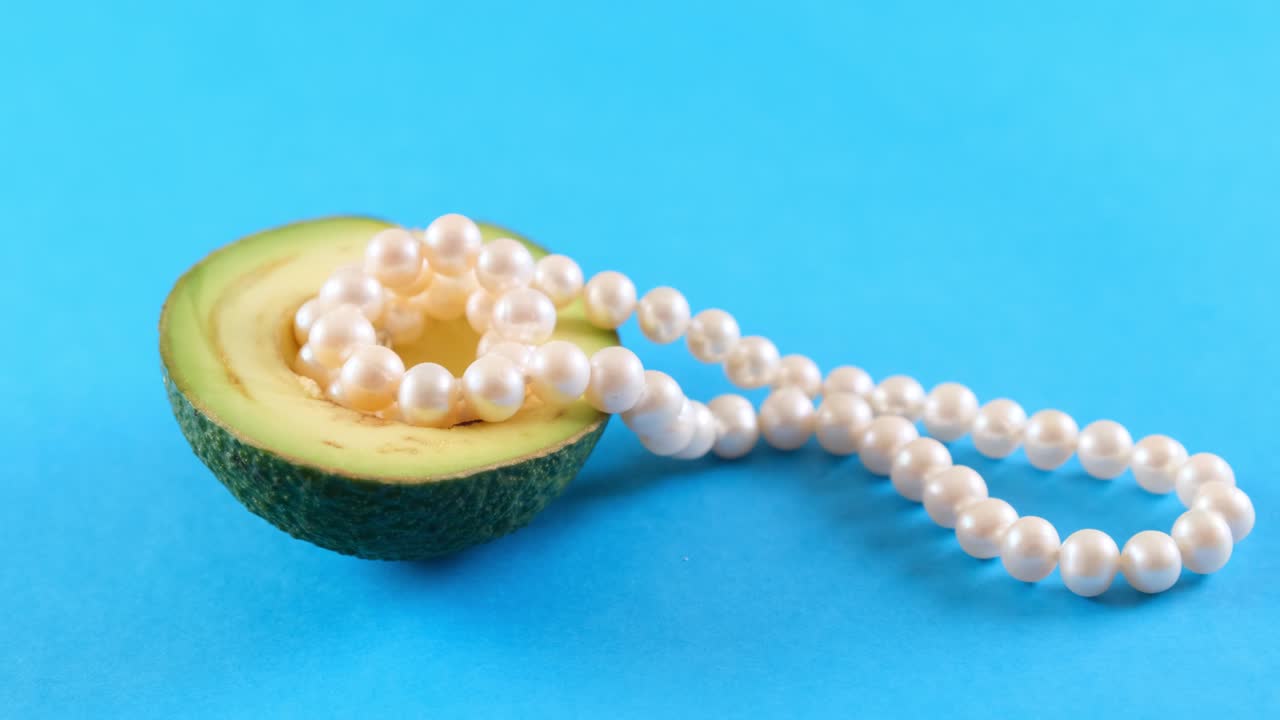 medio fruto de aguacate fresco con perlas en fondo azul. diseño de alimentos de moda