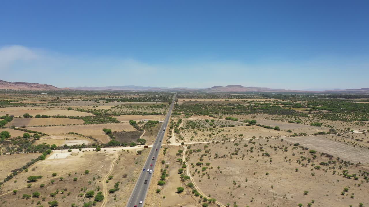Video aereo ad alta quota di un'autostrada messicana con traffico nel deserto, con cielo azzurro e montagne sullo sfondo