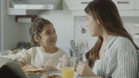 happy mom and little daughter talking and embracing on breakfast at home