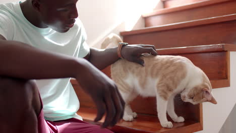 petting cat on stairs, african american man bonding with his pet at home