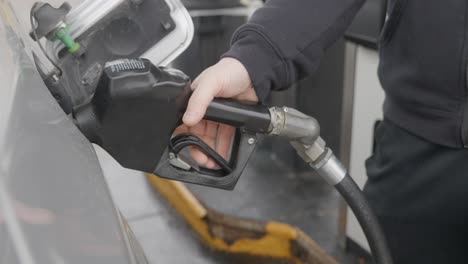 gas station white caucasian man with wedding ring filling up silver car removing inserted gas nozzle from tank and turning towards pump