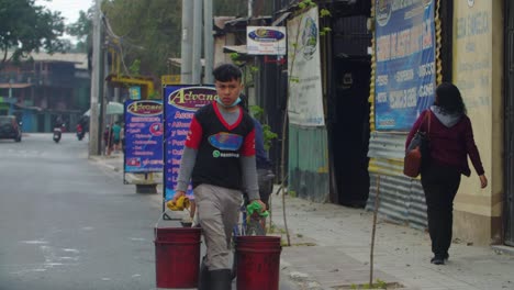 street view of cyclist riding road, people walking sidewalk, young man carrying two buckets, zone 18 guatemala city guatemala - handheld slow motion