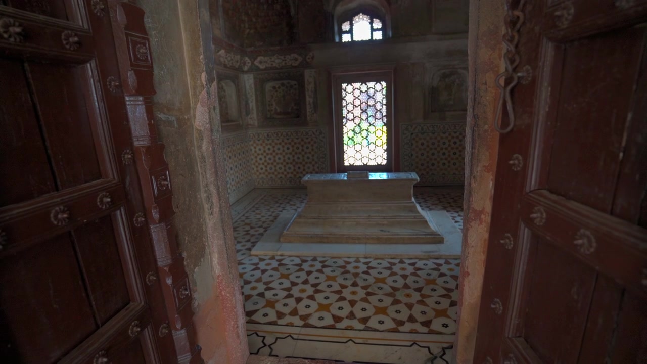 Inquadratura con avvicinamento attraverso porte di legno intagliate aperte che mostra all'interno una tomba cenotafio in marmo bianco nella Tomba di Itimad-ud-Daulah ad Agra, Uttar Pradesh, India