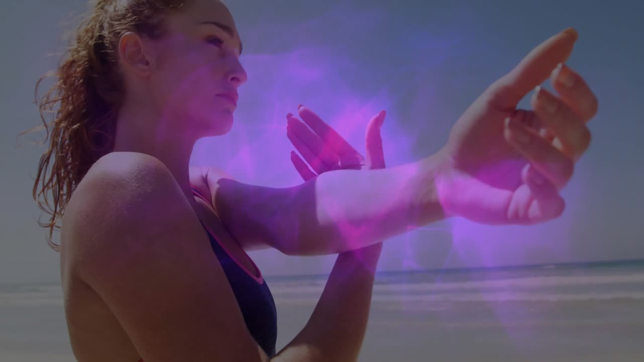 Mulher estendendo o braço na praia, iniciando demonstração de fitness com névoa de energia rosa-púrpura pulsando no antebraço.