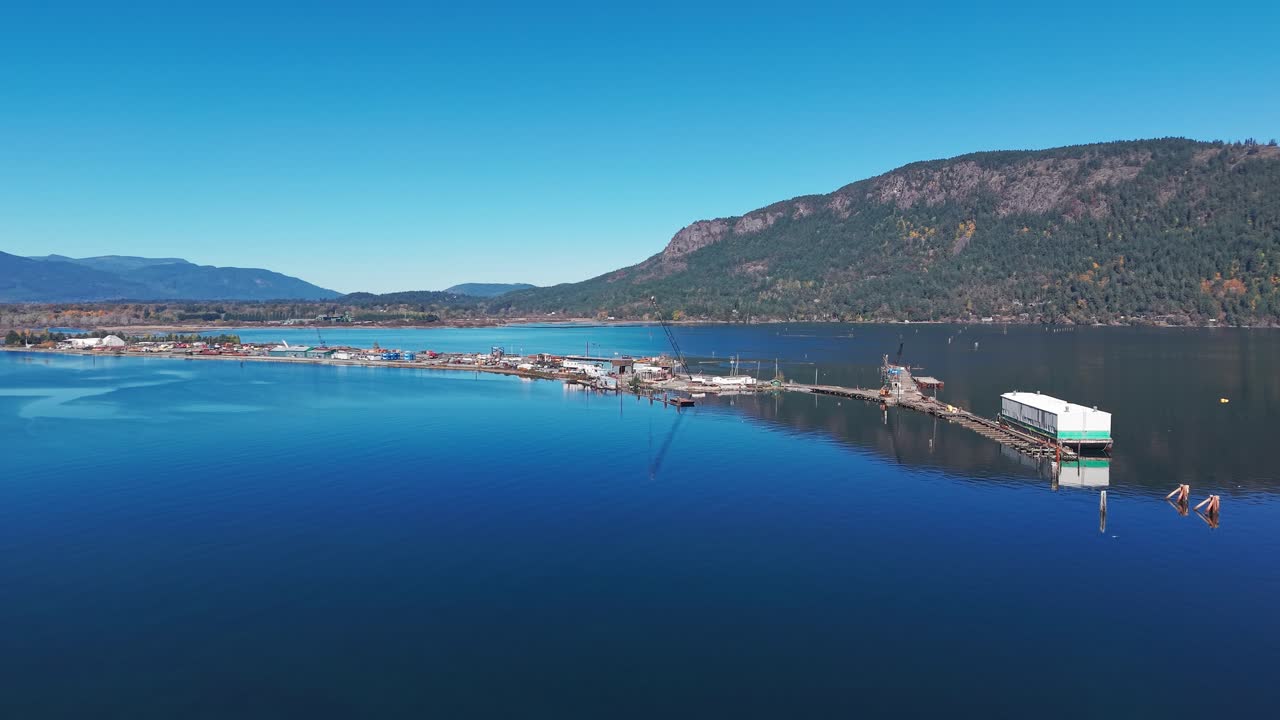Dronebilde av flytende brygger i Cowichan Bay med rolig, blått vann og skogkledde fjell på Vancouver Island, Britisk Columbia under en klar, blå himmel