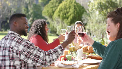 Fröhliche,-Vielfältige-Freunde-Männlicher-Und-Weiblicher-Art-Stoßen-Im-Sonnigen-Garten-Auf-Ein-Festessen-An